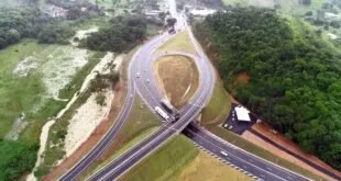 Vista aérea de trevo rodoviário com caminhões trafegando entre áreas verdes