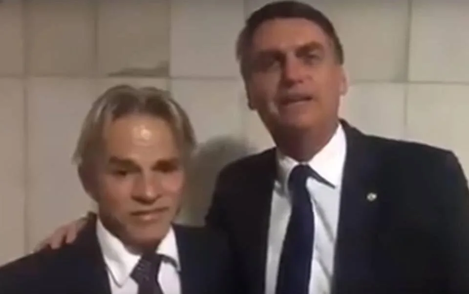 Dois homens de terno lado a lado em quadro de vídeo com fundo escuro