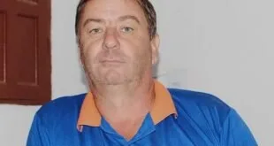 Homem de meia-idade com camisa polo azul e laranja posando diante de parede clara