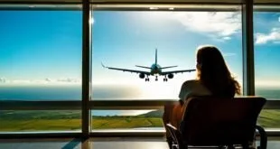 Pessoa sentada em sala de embarque observando avião próximo à janela do aeroporto