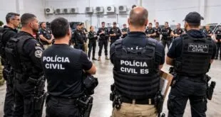 Policiais de costas com coletes escritos 'Polícia Civil ES' reunidos em auditório