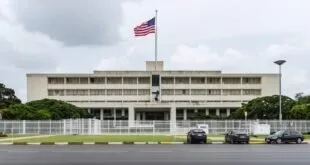Fachada de embaixada com bandeira dos Estados Unidos hasteada e carros estacionados na rua