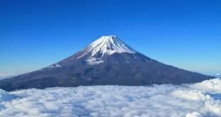 Montanha com cume nevado emergindo de um mar de nuvens sob céu azul