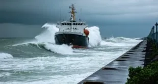 Navio enfrenta ondas fortes ao lado de molhe de concreto sob céu carregado