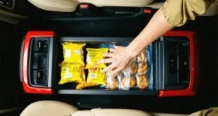 Mão retira pacotes e sacos plásticos de compartimento no console central de um carro