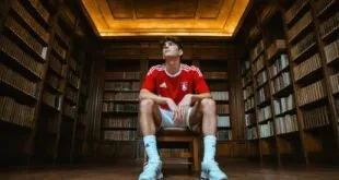 Jovem em uniforme vermelho na biblioteca, símbolo de transferência de Liam Delap