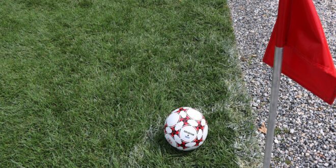 Bola de futebol na linha de cal, ao lado da bandeirinha vermelha de escanteio