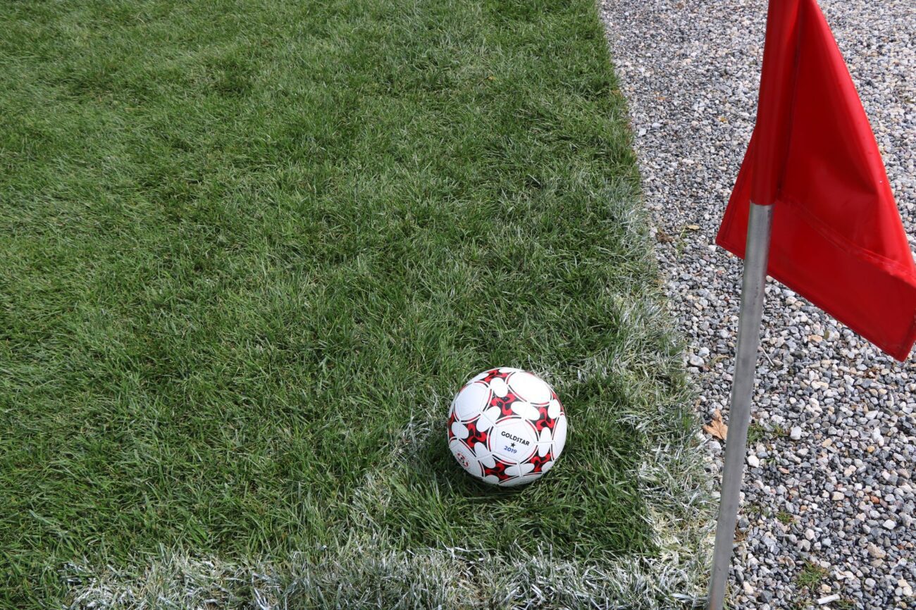 Bola de futebol na linha de cal, ao lado da bandeirinha vermelha de escanteio