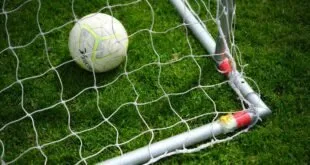 Bola de futebol branca com detalhes em amarelo dentro de uma rede, sobre grama verde, ilustração sobre brasileiro mais caro