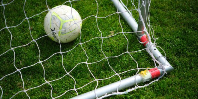 Bola de futebol parada dentro da rede do gol, em campo de grama