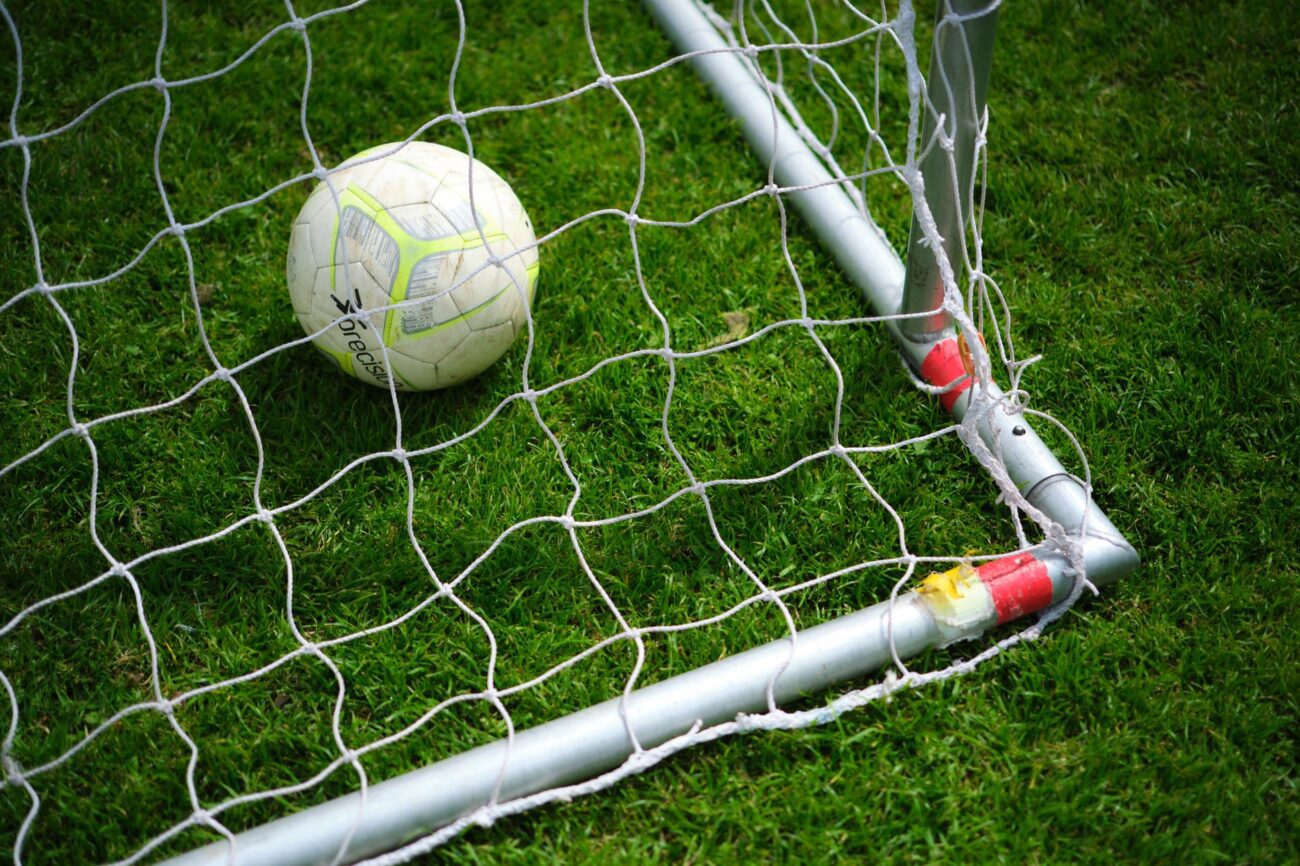 Bola de futebol parada dentro da rede do gol, em campo de grama