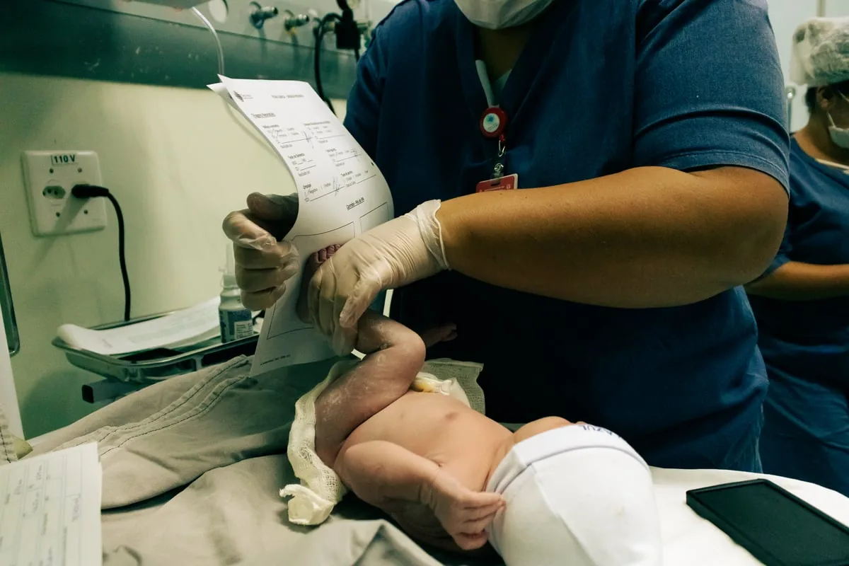 Profissional de saúde realizando o teste do pezinho em bebê recém-nascido em maternidade