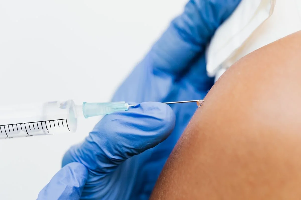 Profissional de saúde aplica vacina no braço de paciente em posto de saúde