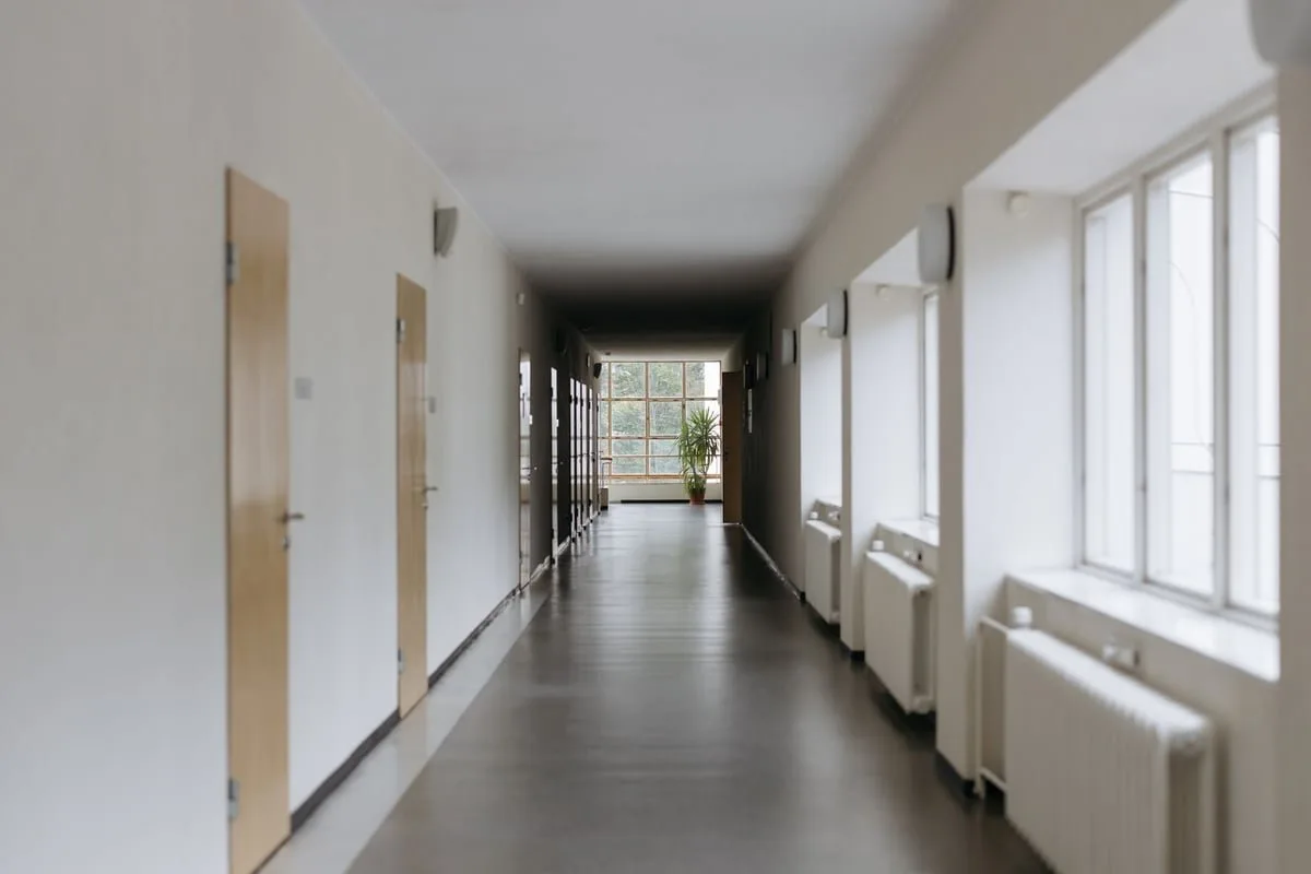 Corredor de escola com mesas e cadeiras vazias, iluminado por luz natural
