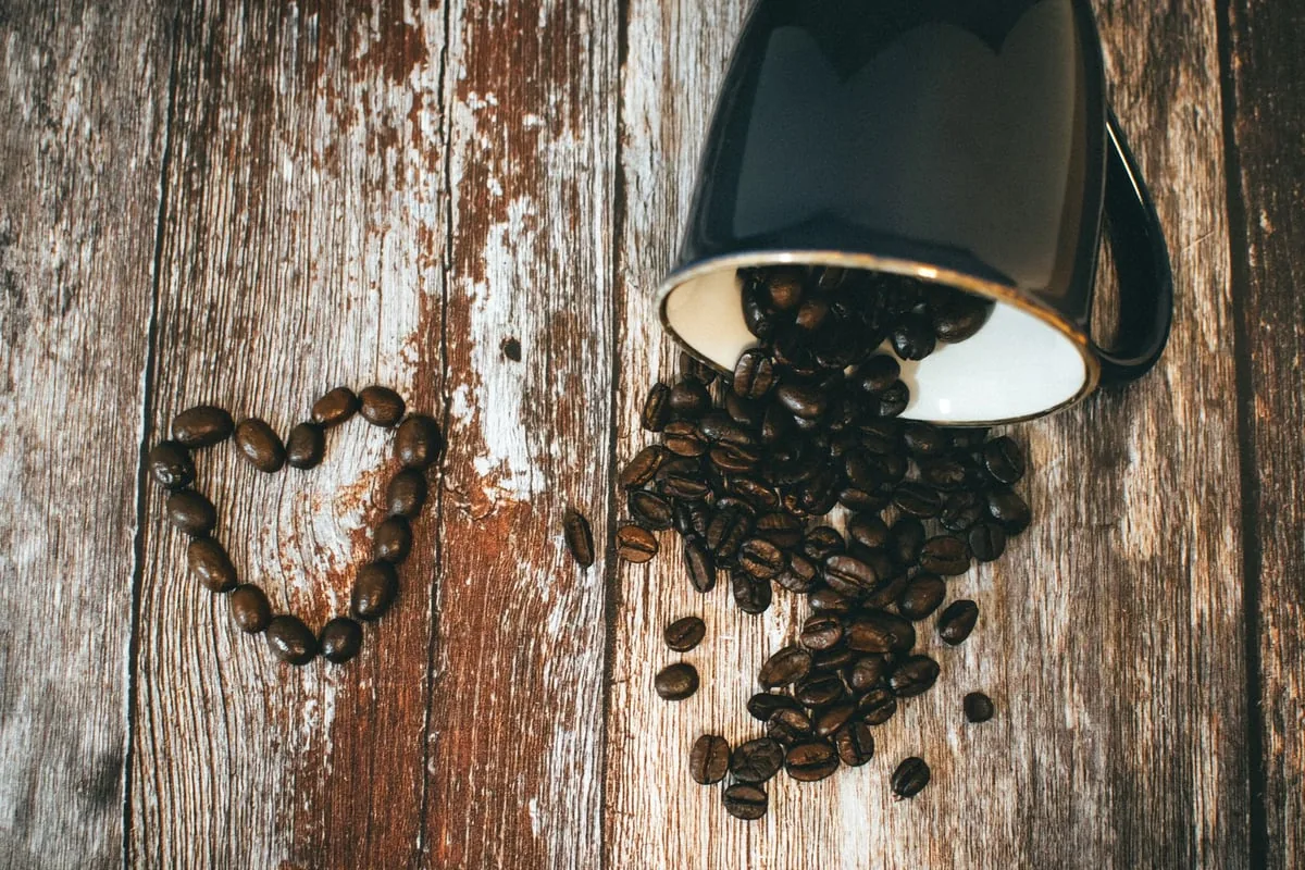 Grãos de café torrados e uma xícara de café sobre uma mesa de madeira