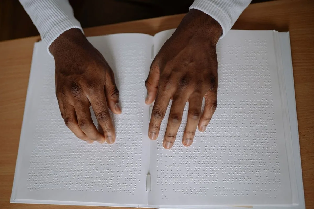 Mão lendo texto em braille com os dedos sobre página com pontos em relevo