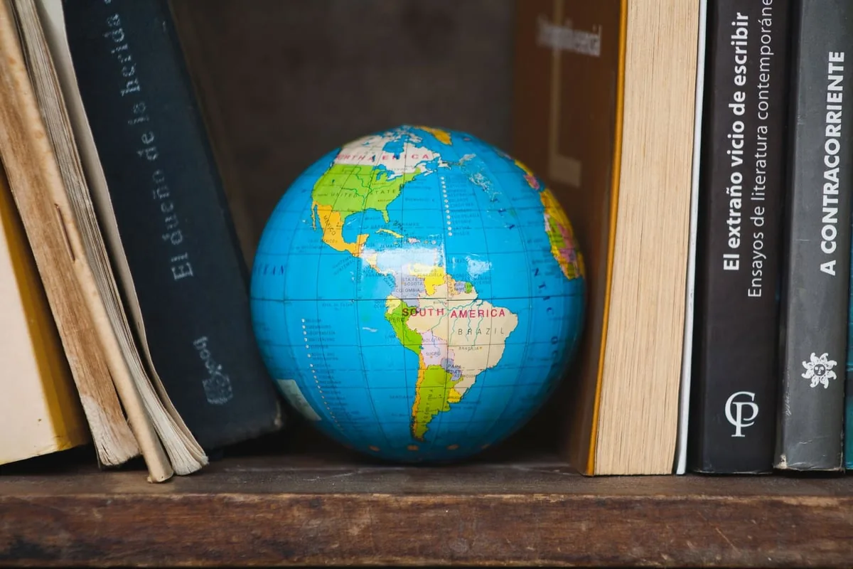 livro antigo aberto ao lado de globo terrestre e microscópio sobre mesa de estudo