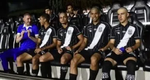 Jovens da base conversam no banco de reservas com uniformes preto e branco durante partida