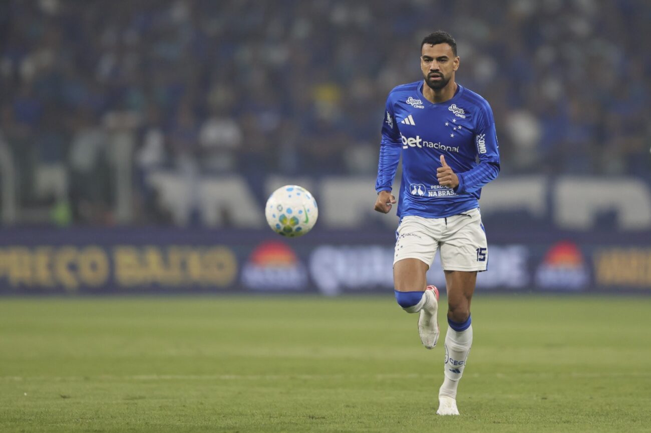 Jogador de futebol em uniforme azul e branco corre atrás da bola em campo durante partida