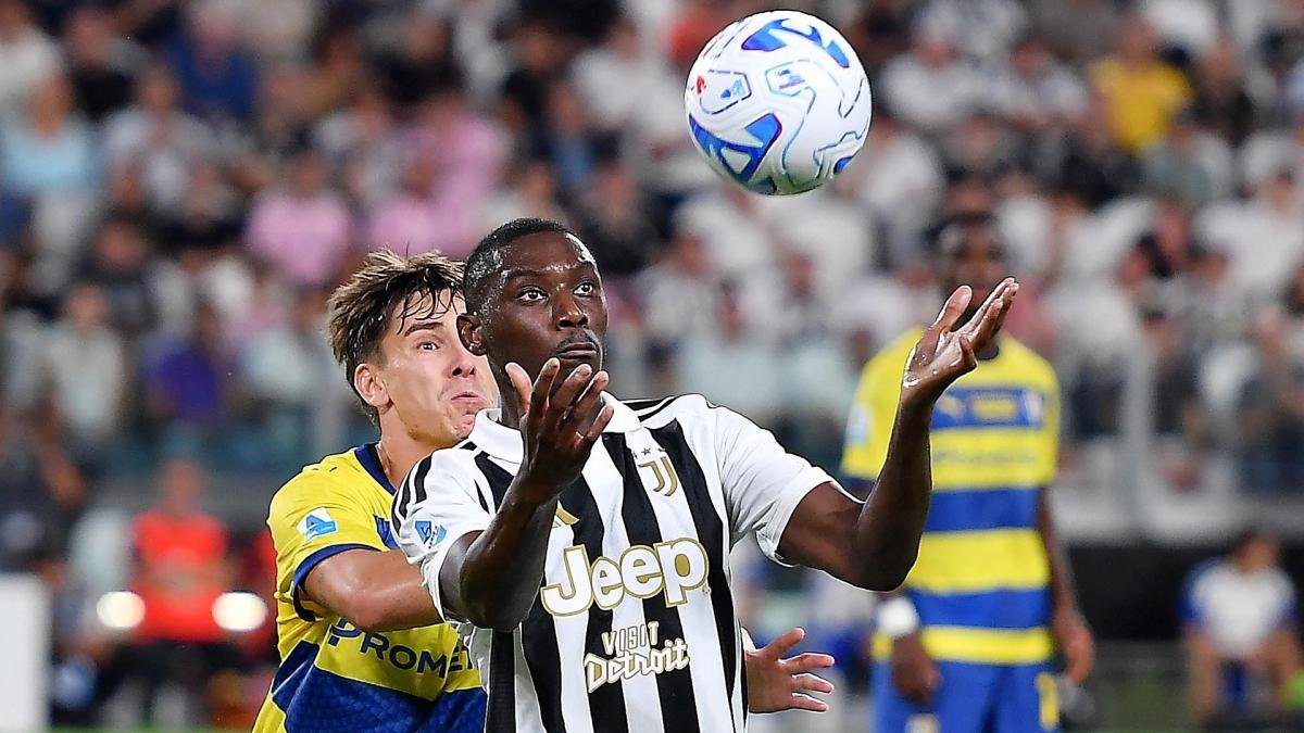 Dois jogadores disputam a bola durante uma partida de futebol em estádio com torcida ao fundo