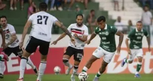 Bola de futebol em campo deste sábado com torcida ao fundo