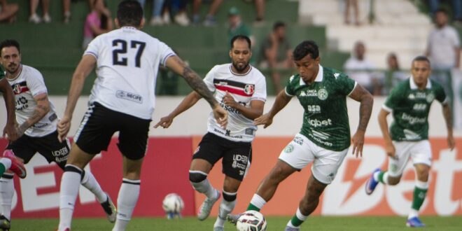 Bola de futebol em campo deste sábado com torcida ao fundo