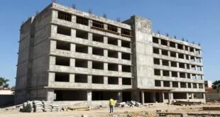 Trabalhador em colete amarelo observa construção de prédio de concreto inacabado sob céu azul