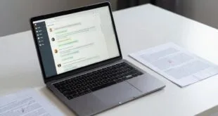 Laptop aberto em mesa branca com aplicativo de mensagens na tela e documentos impressos ao lado