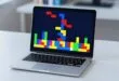 Notebook com jogo Tetris Casa Branca em blocos coloridos sobre mesa branca
