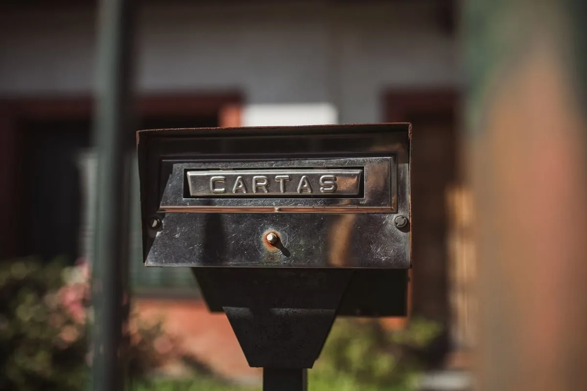 Caixa de correio antiga de metal fixada em muro, com cartas parcialmente visíveis