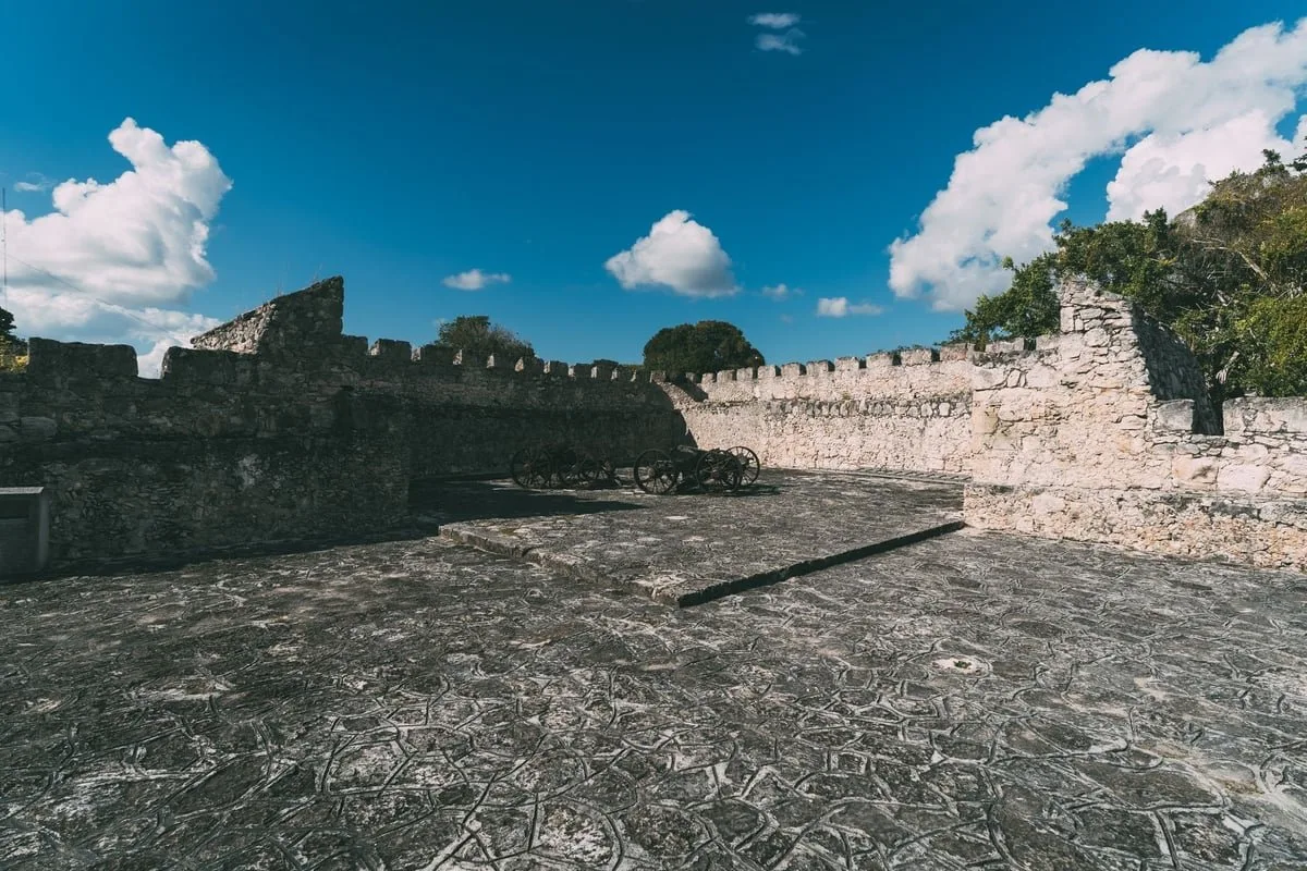 Muro de fortificação antiga de pedra sob céu claro, com poste de execução histórica ao centro