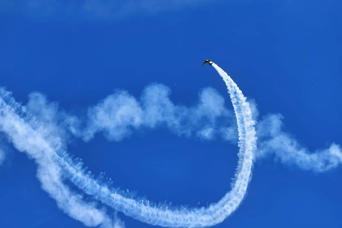 Avião de exibição solta rastros de fumaça colorida durante manobra acrobática no céu azul
