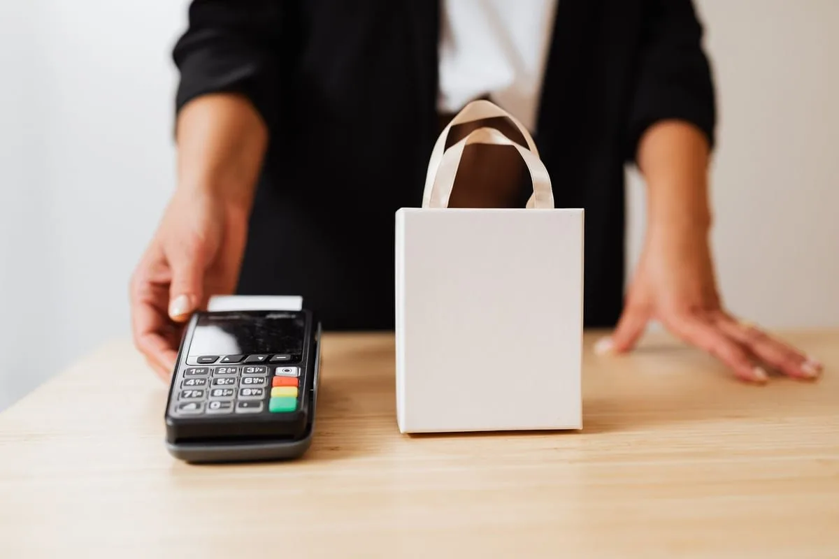 vendedora entregando sacola de compras para cliente em loja