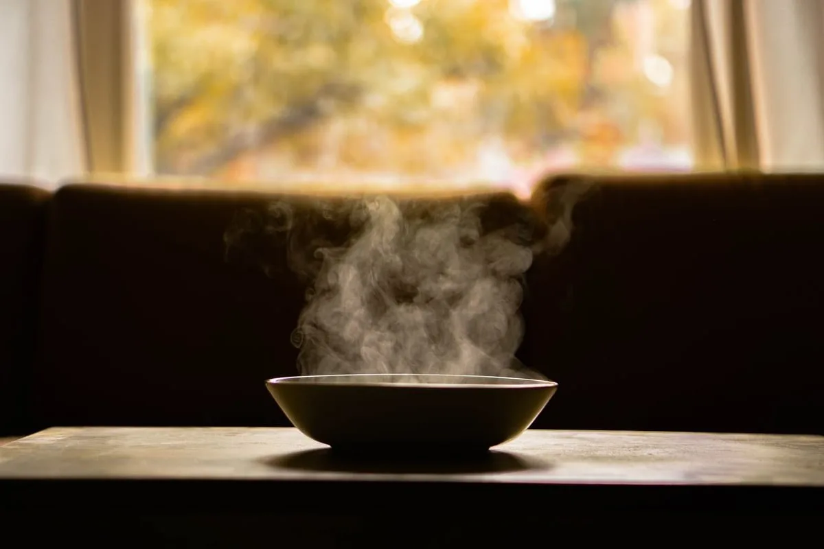 Mãos idosas segurando tigela de sopa em ambiente simples de acolhimento