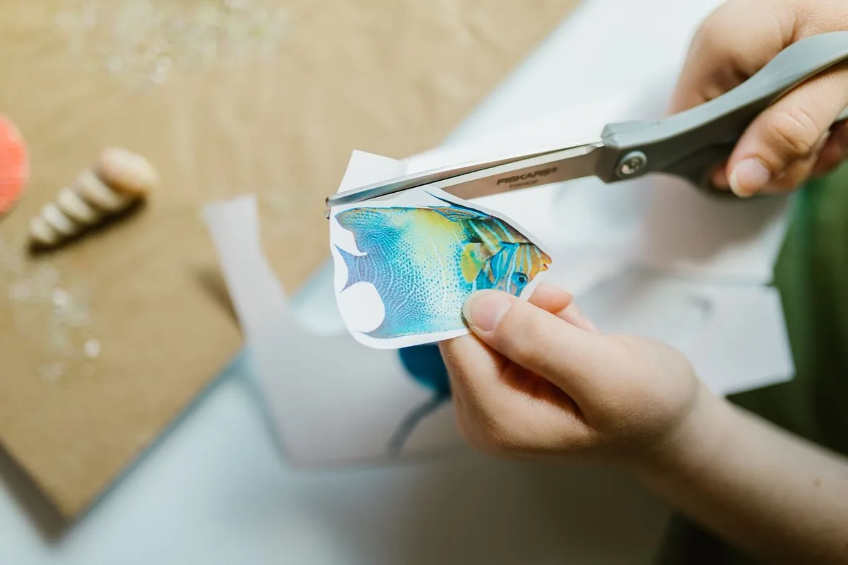 Mão segurando peixe de papel colorido recortado sobre fundo neutro