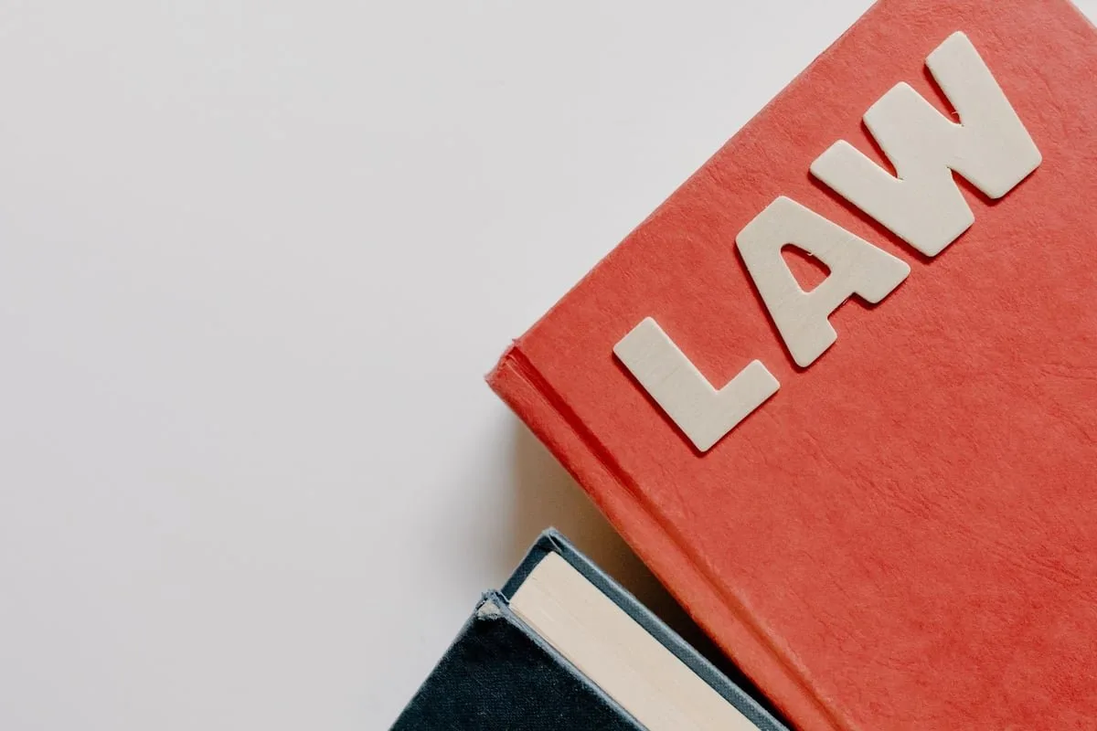 Livro de leis grosso aberto sobre mesa de escritório com óculos ao lado