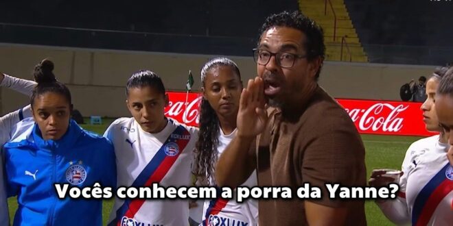 Homem de óculos e casaco marrom fala para grupo de mulheres em uniforme de futebol em campo com publicidade