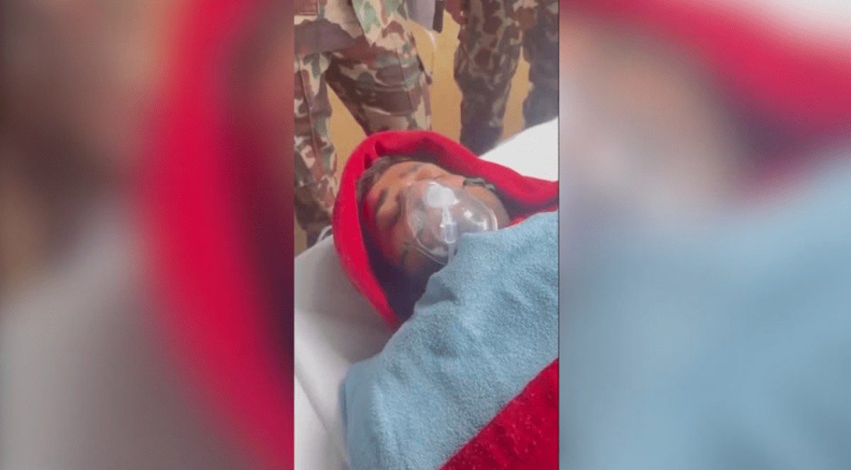 Bebê recém-nascido envolto em pano vermelho e branco, sendo segurado por uma pessoa em ambiente interno