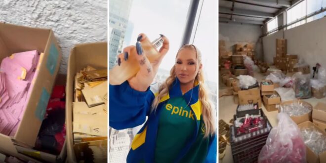 Mulher em armazém mostra frasco de produto com unhas decoradas, cercada por caixas e embalagens
