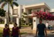 Rua de bairro com mansão mais cara do Brasil, flores rosa, palmeiras e portão de ferro