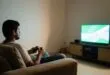 Pessoa com controle de videogame assistindo TV na sala, usando game pass