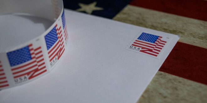 Selo postal com bandeira dos EUA em envelope branco, simbolizando patriotismo, ilustração sobre voto pelo correio nos EUA