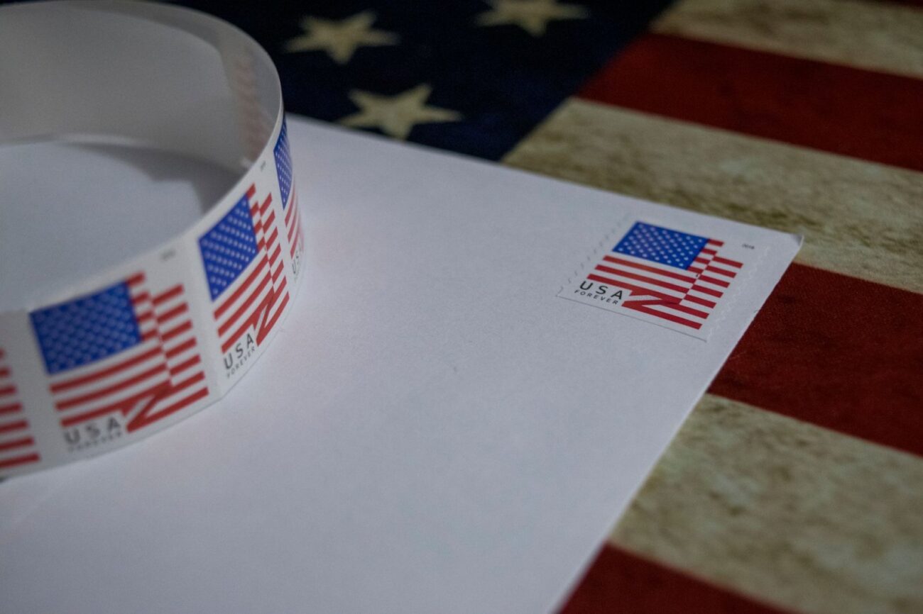 Selo postal com bandeira dos EUA em envelope branco, simbolizando patriotismo, ilustração sobre voto pelo correio nos EUA