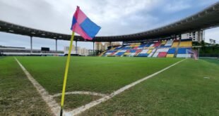 Bandeira de escanteio em gramado de estádio vazio com arquibancada colorida ao fundo