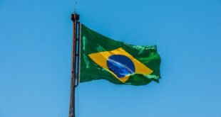 Bandeira do Brasil hasteada em mastro tremulando contra o céu azul