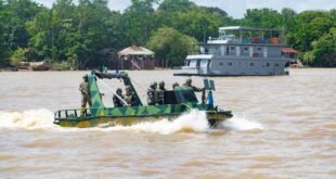 Militares armados em embarcação camuflada navegando em rio com barco de apoio ao fundo