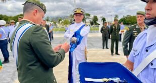 Militar cumprimenta oficial de uniforme branco ao lado de mesa com medalhas e espadas
