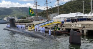 Submarino atracado em cais com marinheiros em formação sobre o casco