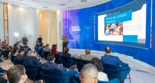 Militar apresenta palestra para plateia sentada em poltronas diante de painel de LED