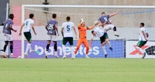 Disputa de bola pelo alto na pequena área com goleiro de uniforme laranja observando